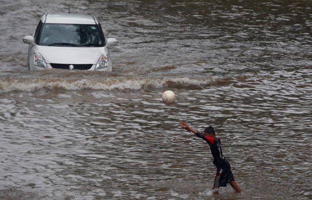 Un ragazzo gioca mentre una macchina attraversa una strada allagata durante le piogge monsoniche di Mumbai, in India il 10 giugno 2013. Le forti piogge hanno interrotto il traffico ferroviario e stradale nella capitale commerciale dell'India. (Rafiq Maqbool / Associated Press)