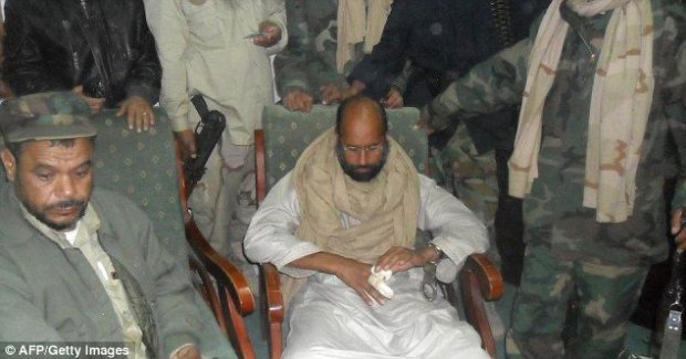 Scared: Saif looks nervous as he sits surrounded by his rebel captors, and he looks at his injured hand